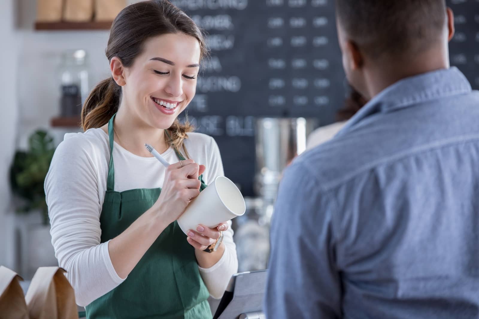 Cheerful coffee shop barista writes order on cup